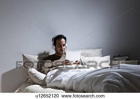 Stock Image - Man using tablet computer in bed. Fotosearch