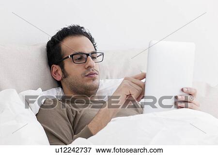 Stock Photo - Man using tablet computer in bed. Fotosearch
