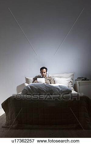 Stock Photo - Man using tablet computer in bed. Fotosearch