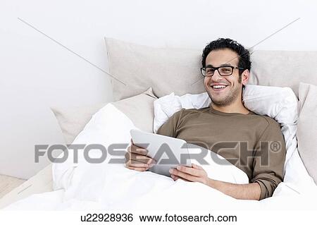 Man using tablet computer in bed View Large Photo Image Stock Photograph - Man using tablet computer in bed. Fotosearch