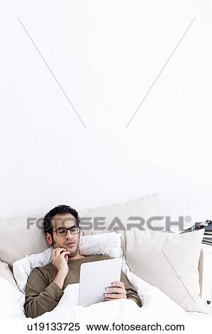 Stock Photography - Man using tablet computer in bed. Fotosearch