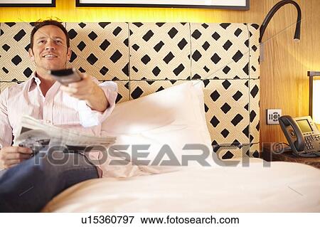 Stock Photo - Man watching television on bed. Fotosearch