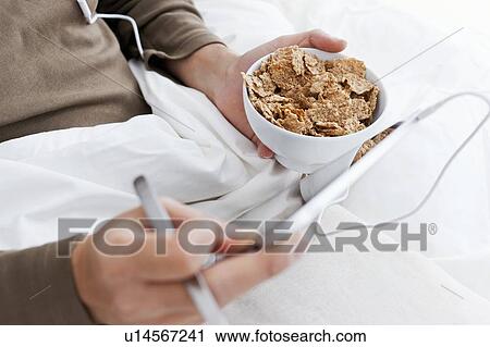 Stock Image - Man with tablet computer eating in bed. Fotosearch