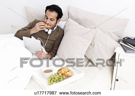 Man with tablet computer eating in bed View Large Photo Image Stock Photo - Man with tablet computer eating in bed. Fotosearch