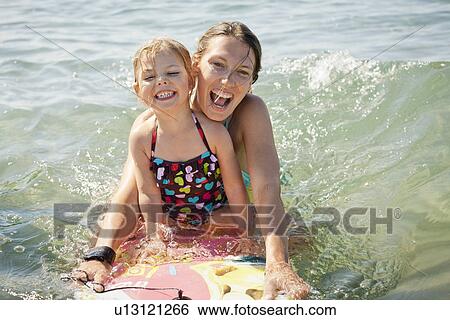 Stock Photograph - Mother and daughter boarding in ocean. Fotosearch