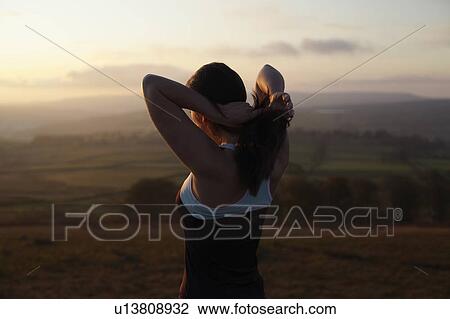 Stock Image - Runner tying her hair in rural landscape. Fotosearch