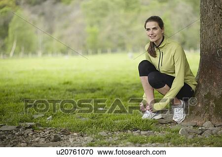 Stock Image - Runner tying her shoes in rural field. Fotosearch