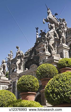Stock Image - Shrubs with ornate statues and columns. Fotosearch