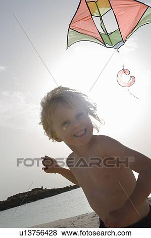 Stock Photo - Smiling boy flying kite on beach. Fotosearch
