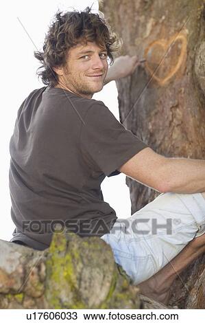 Stock Image - Smiling man carving heart in tree. Fotosearch