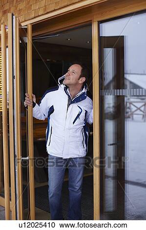 Stock Image - Smiling man looking out glass door. Fotosearch