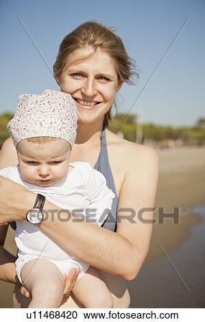 Stock Image - Smiling mother holding baby on beach. Fotosearch