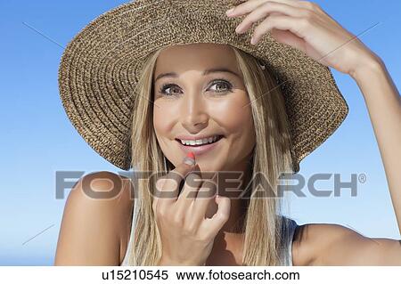 Stock Photography - Smiling woman applying lipstick outdoors. Fotosearch