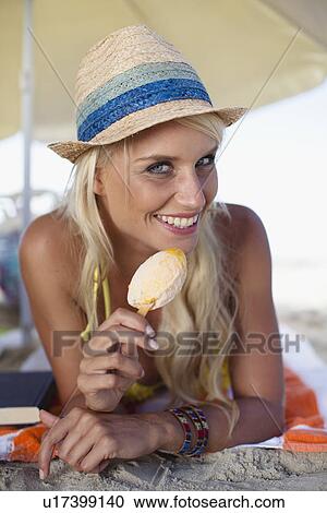 Stock Image - Smiling woman eating popsicle on beach. Fotosearch