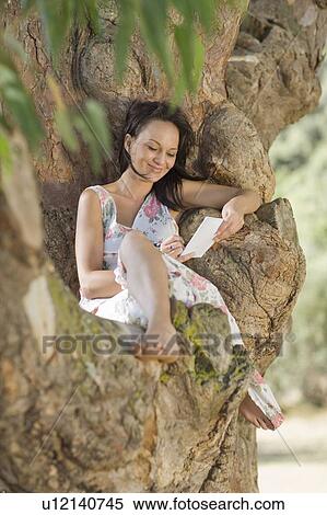 Stock Photography - Smiling woman reading in tree. Fotosearch