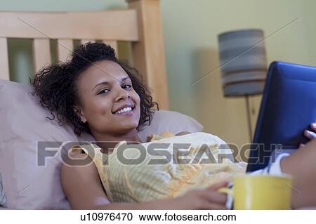 Stock Image - Smiling woman reading on bed. Fotosearch