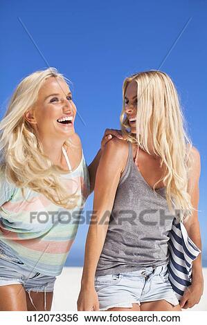 Stock Photograph - Smiling women walking together on beach. Fotosearch