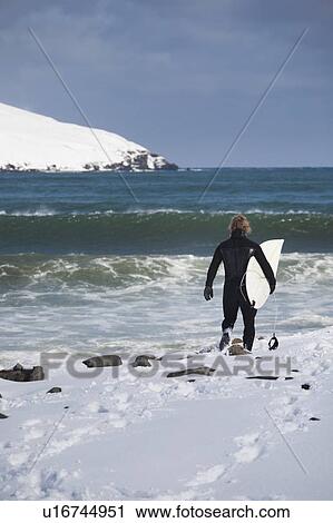 Surfer carrying surfboard on snowy beach View Large Photo Image Stock Image - Surfer carrying surfboard on snowy beach. Fotosearch