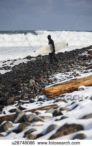 Surfer carrying surfboard on snowy beach View Large Photo Image Stock Photograph - Surfer carrying surfboard on snowy beach. Fotosearch