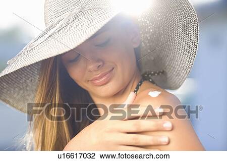 Stock Image - Teenage girl applying sunscreen outdoors. Fotosearch