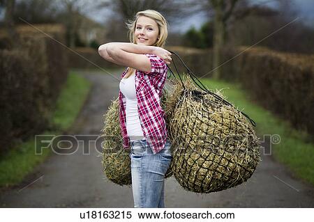Stock Photography - Teenage girl carrying hay on dirt path. Fotosearch