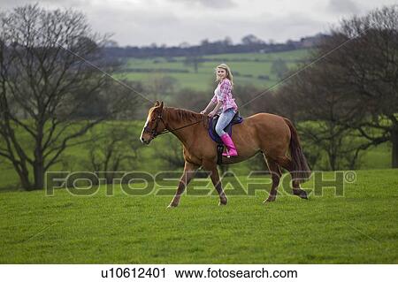 Stock Image - Teenage girl riding horse in field. Fotosearch