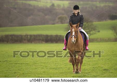 Stock Photo - Teenage girl riding horse in field. Fotosearch