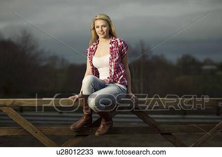 Stock Image - Teenage girl sitting on wooden fence. Fotosearch