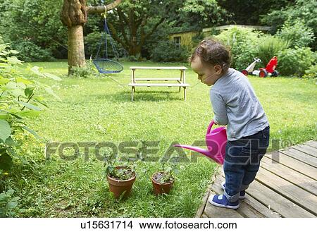 Toddler boy watering plants in backyard View Large Photo Image Picture - Toddler boy watering plants in backyard. Fotosearch