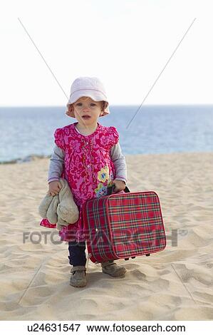 Stock Photo - Toddler carrying suitcase on beach. Fotosearch