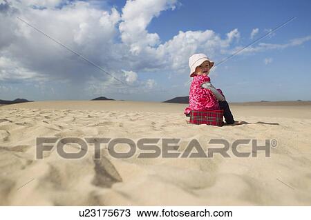 Stock Image - Toddler sitting on suitcase on beach. Fotosearch