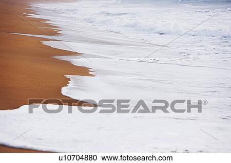 Stock Image - Waves washing up on sandy beach. Fotosearch