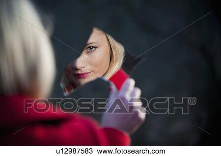Stock Image - Woman admiring herself in mirror shard. Fotosearch