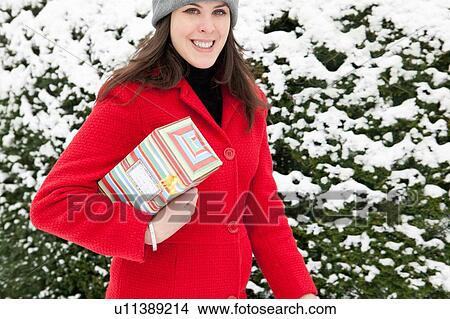 Picture - Woman carrying wrapped gift in snow. Fotosearch