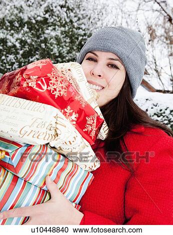 Stock Image - Woman carrying wrapped gifts in snow. Fotosearch