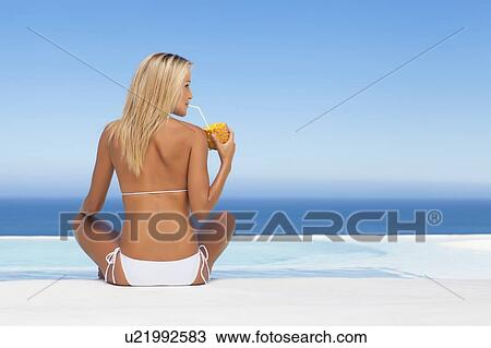 Stock Image - Woman drinking from pineapple by pool. Fotosearch