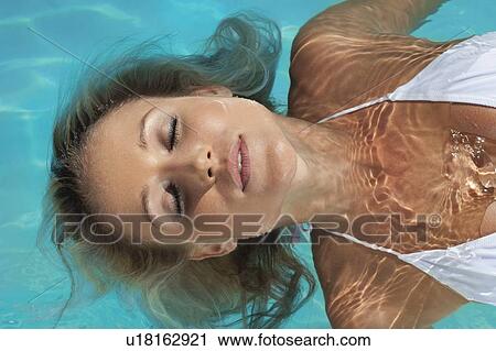 Stock Image - Woman floating in swimming pool. Fotosearch