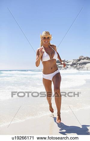 Stock Image - Woman in bikini running on beach. Fotosearch