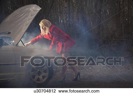 Stock Image - Woman looking under hood of car at night. Fotosearch