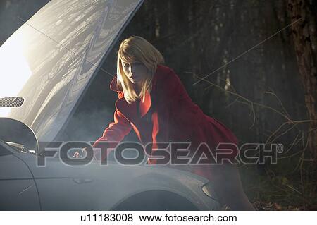 Stock Photo - Woman looking under hood of car at night. Fotosearch