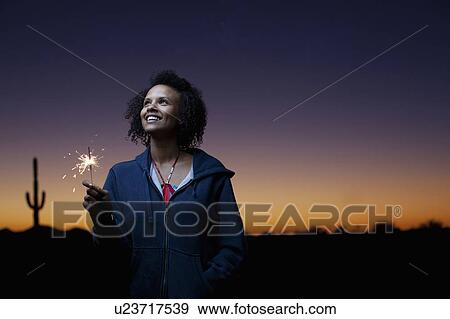 Stock Photo - Woman playing with sparkler in desert. Fotosearch