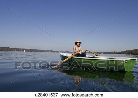 Stock Photo - Woman rowing boat in still lake. Fotosearch