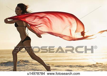 Picture - Woman running with sarong on beach. Fotosearch