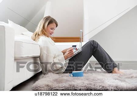 Stock Image - Woman shopping online in living room. Fotosearch