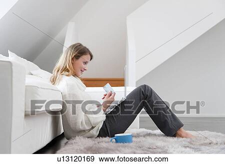 Stock Photo - Woman shopping online in living room. Fotosearch