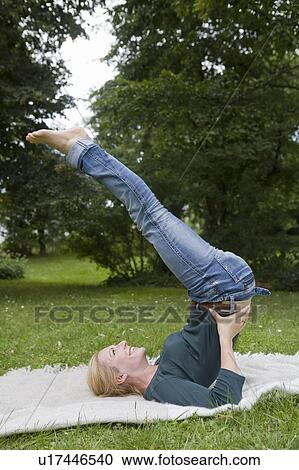 Stock Image - Woman stretching on blanket in grass. Fotosearch