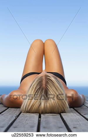 Stock Image - Woman sunbathing on wooden pier. Fotosearch
