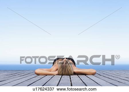 Stock Photo - Woman sunbathing on wooden pier. Fotosearch