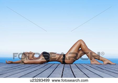 Stock Photo - Woman sunbathing on wooden pier. Fotosearch