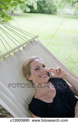Stock Image - Woman talking on cell phone in hammock. Fotosearch